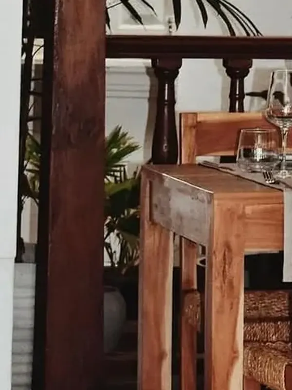 Teak column and carved balustrade in the Malu dining room, with a laid table, wine glasses and a woven chair